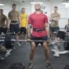 Mann-hebt-gewichte-mit-einer-Gruppe-sportler-im-Fitnesstudio